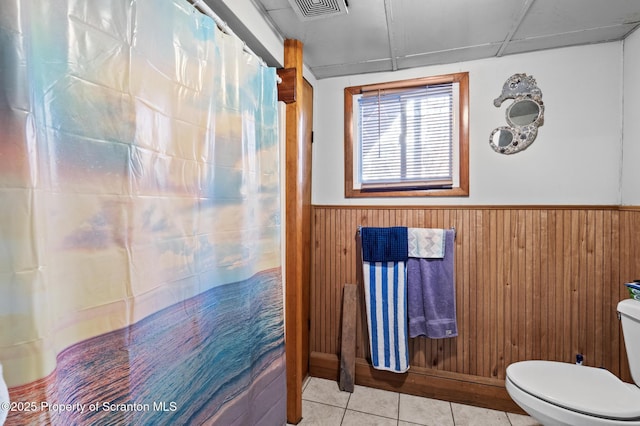 bathroom with wooden walls, visible vents, toilet, a wainscoted wall, and tile patterned floors