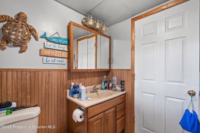 half bath with toilet, wainscoting, vanity, and wooden walls