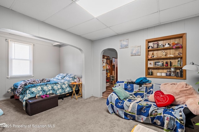 carpeted bedroom with arched walkways and a drop ceiling