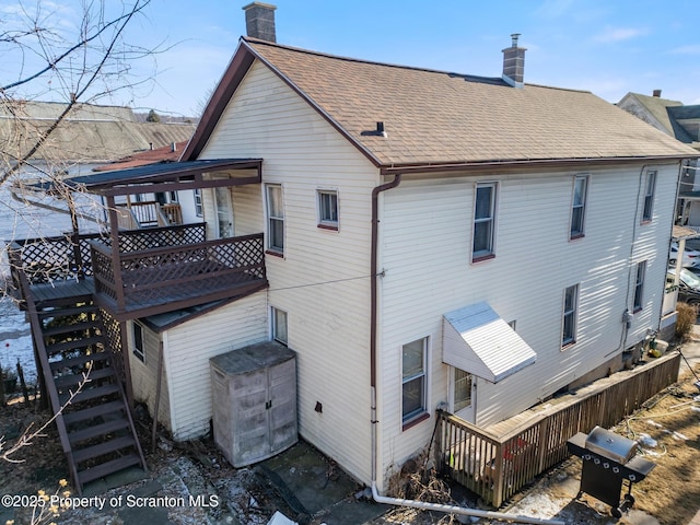 back of property with stairway, a shingled roof, a chimney, and a wooden deck