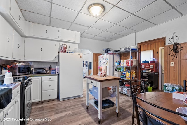 kitchen featuring arched walkways, stainless steel appliances, white cabinetry, light wood-type flooring, and a drop ceiling