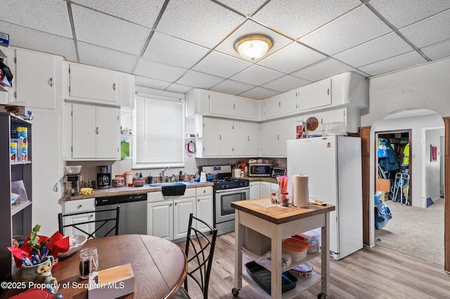 kitchen with a sink, white cabinetry, stainless steel appliances, and arched walkways