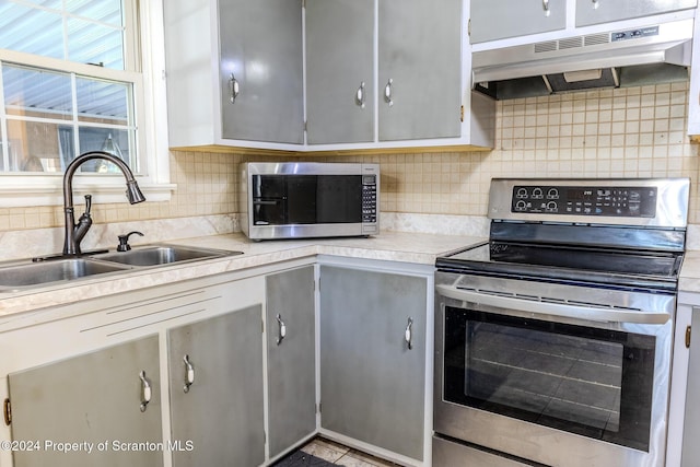 kitchen with decorative backsplash, appliances with stainless steel finishes, gray cabinetry, sink, and exhaust hood