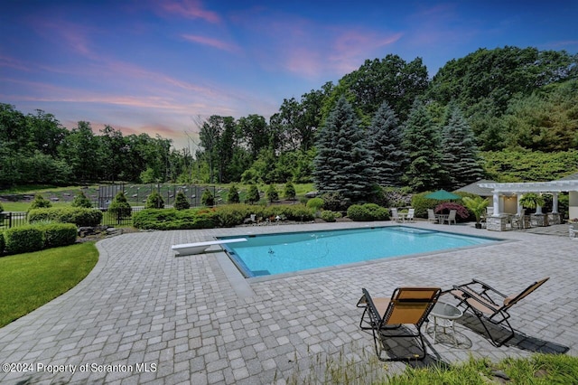 pool at dusk featuring a patio area and a diving board