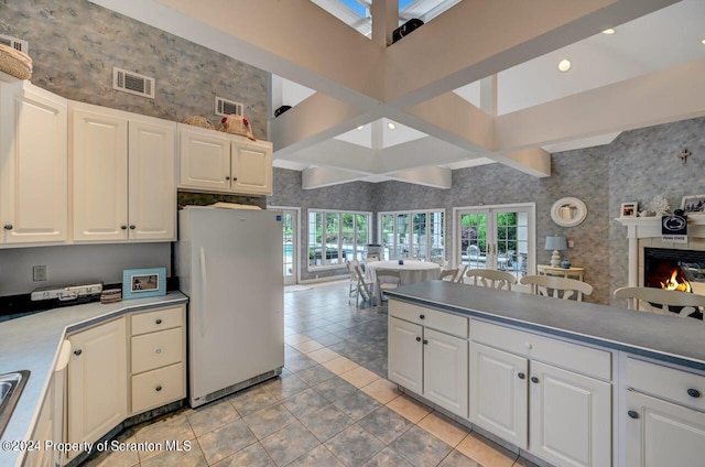 kitchen with light tile patterned floors, white fridge, white cabinetry, and a tiled fireplace