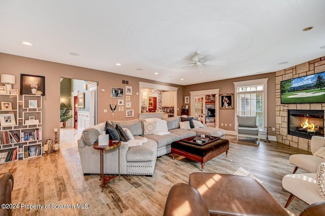 living room featuring light hardwood / wood-style flooring, a stone fireplace, and ceiling fan