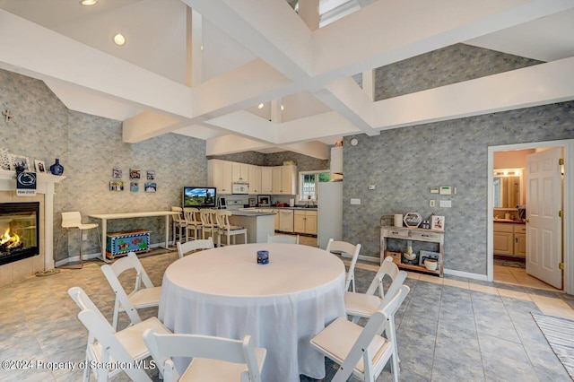 dining room featuring a fireplace, light tile patterned floors, a towering ceiling, and beam ceiling