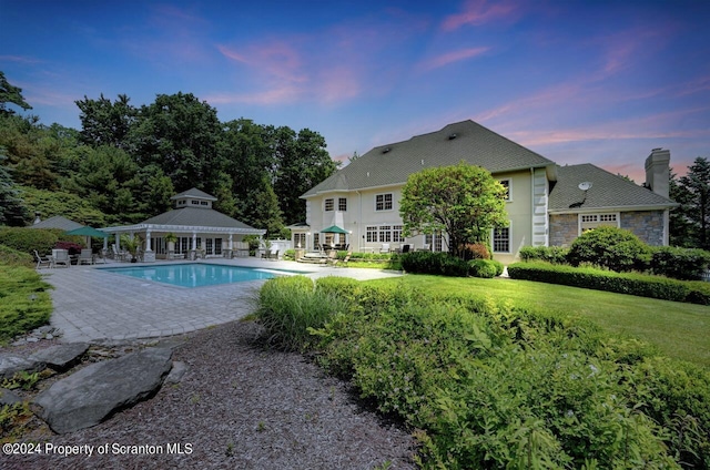 pool at dusk featuring a patio area and a yard