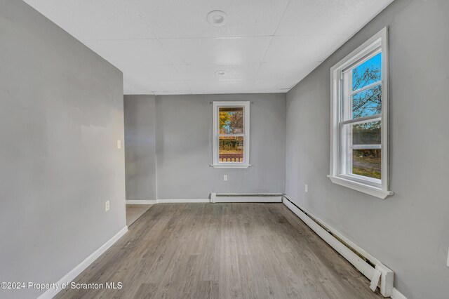 empty room featuring a paneled ceiling, light hardwood / wood-style floors, and baseboard heating