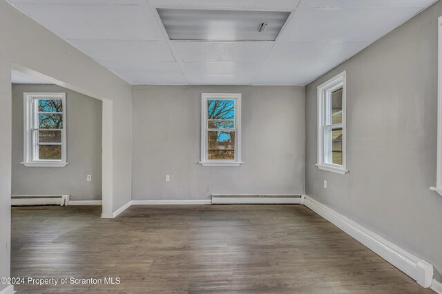 unfurnished room with hardwood / wood-style floors, a paneled ceiling, a wealth of natural light, and baseboard heating