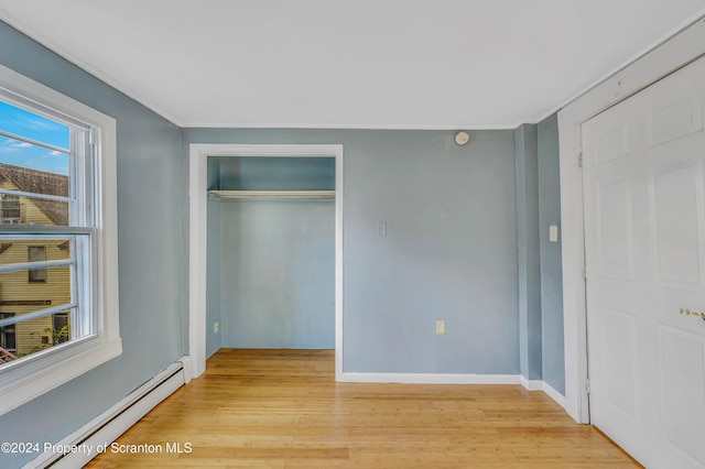 unfurnished bedroom with a closet, light hardwood / wood-style flooring, and a baseboard heating unit