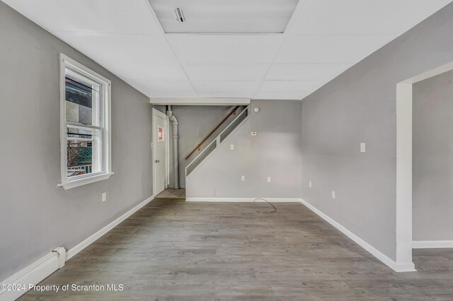 basement with a paneled ceiling, baseboard heating, and hardwood / wood-style floors