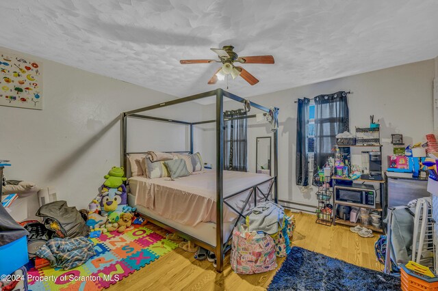 bedroom featuring hardwood / wood-style floors, ceiling fan, baseboard heating, and a textured ceiling