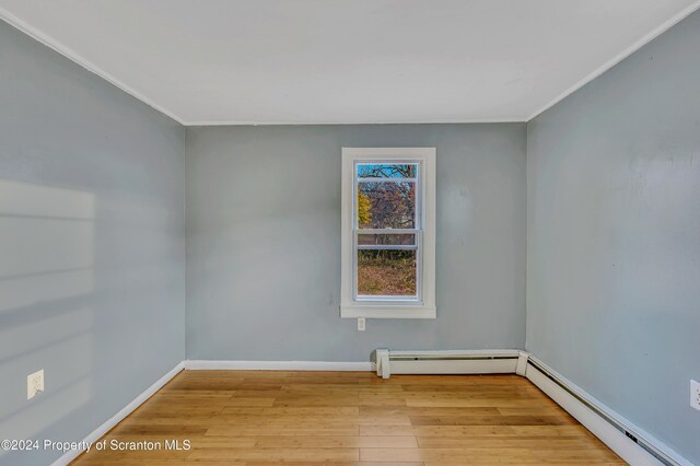 unfurnished room featuring light wood-type flooring, a baseboard radiator, and ornamental molding