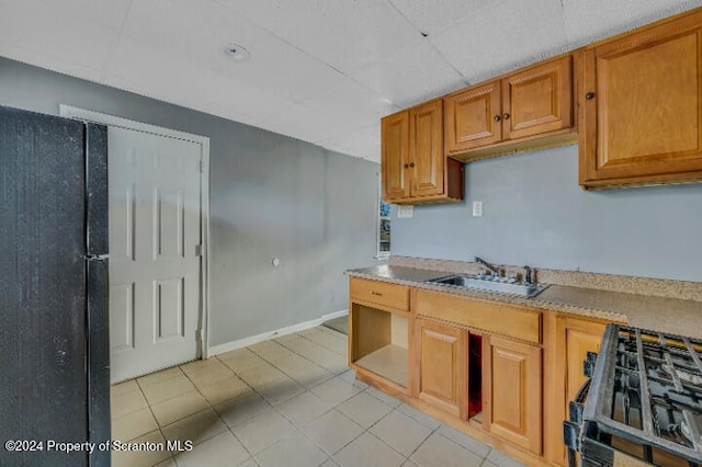 kitchen with sink, black fridge, a drop ceiling, and range with gas stovetop