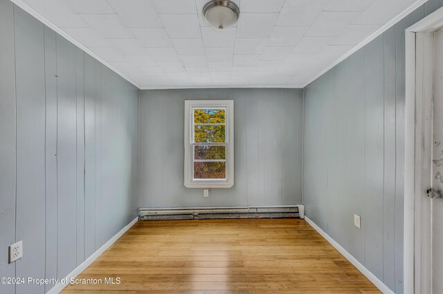 empty room with wood-type flooring, crown molding, and a baseboard heating unit