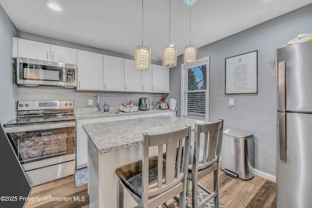 kitchen with a kitchen bar, white cabinetry, decorative light fixtures, appliances with stainless steel finishes, and light hardwood / wood-style floors