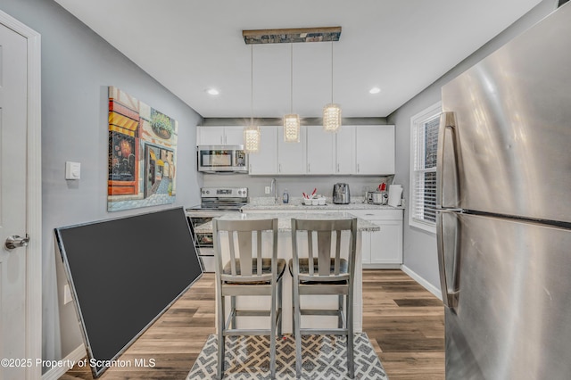 kitchen featuring hardwood / wood-style floors, decorative light fixtures, white cabinets, light stone counters, and stainless steel appliances