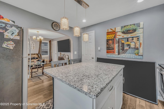 kitchen with decorative light fixtures, a center island, stainless steel fridge, light hardwood / wood-style floors, and white cabinets