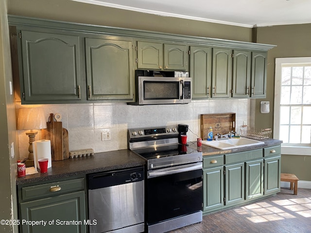 kitchen featuring a sink, backsplash, stainless steel appliances, crown molding, and green cabinetry