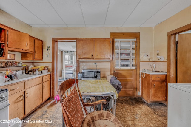 kitchen with a paneled ceiling, washer / clothes dryer, light countertops, stainless steel microwave, and a tiled fireplace