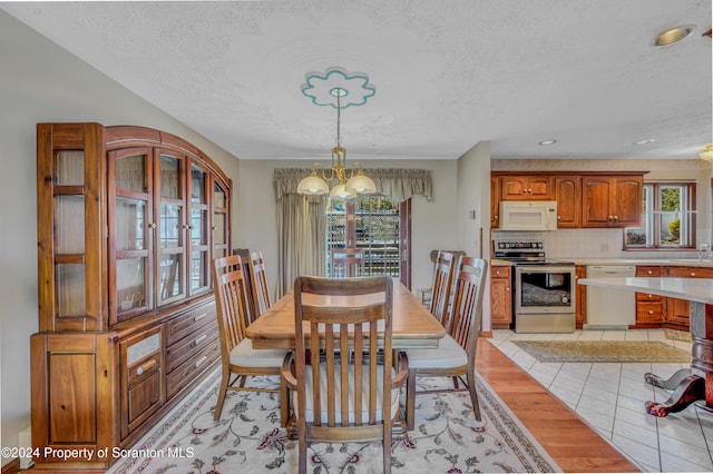 dining space with light hardwood / wood-style flooring, sink, a textured ceiling, and a chandelier