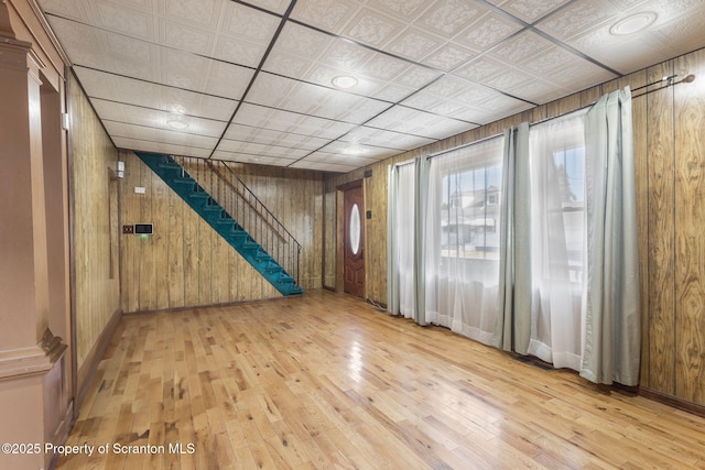 unfurnished room with wooden walls, stairs, baseboards, and hardwood / wood-style flooring