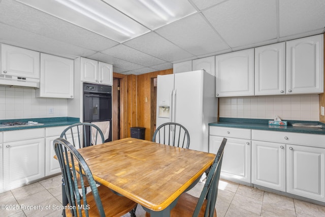 kitchen featuring under cabinet range hood, a drop ceiling, backsplash, white appliances, and white cabinets