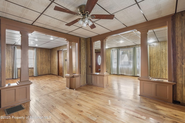 interior space with a wealth of natural light, visible vents, wood-type flooring, ceiling fan, and ornate columns