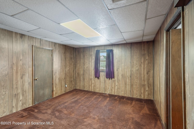 spare room with a drop ceiling, carpet floors, and wooden walls