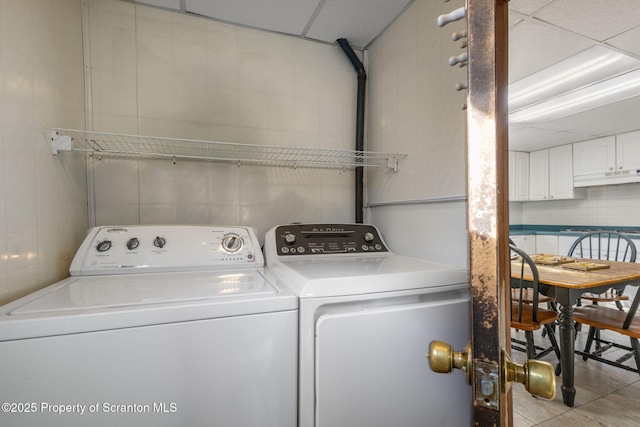 laundry area with washer and dryer, laundry area, light tile patterned flooring, and tile walls