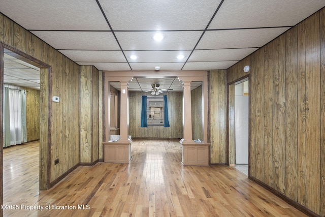 hallway with wood walls, light wood-style floors, and ornate columns