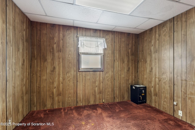 carpeted empty room with a drop ceiling and wood walls