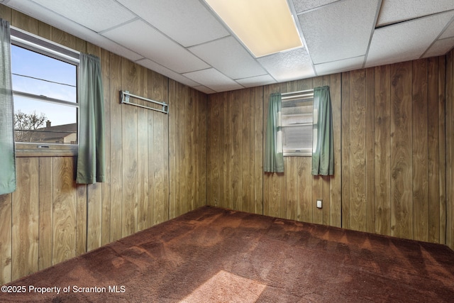 empty room featuring a paneled ceiling, carpet floors, plenty of natural light, and wood walls