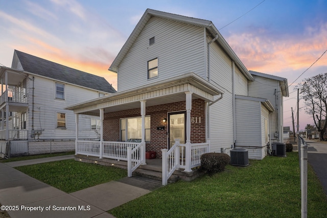 view of front facade featuring central AC unit, a lawn, a porch, and fence