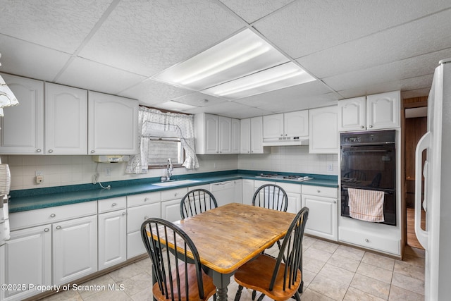 kitchen featuring under cabinet range hood, decorative backsplash, white appliances, white cabinetry, and a sink