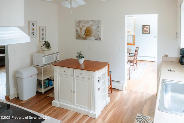 118 Howard St, Old Forge, PA 18518 - kitchen featuring white microwave, light wood-style floors, a ceiling fan, a baseboard radiator, and white cabinetry