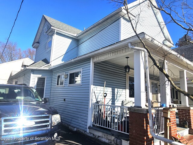 view of side of property with a porch and roof with shingles