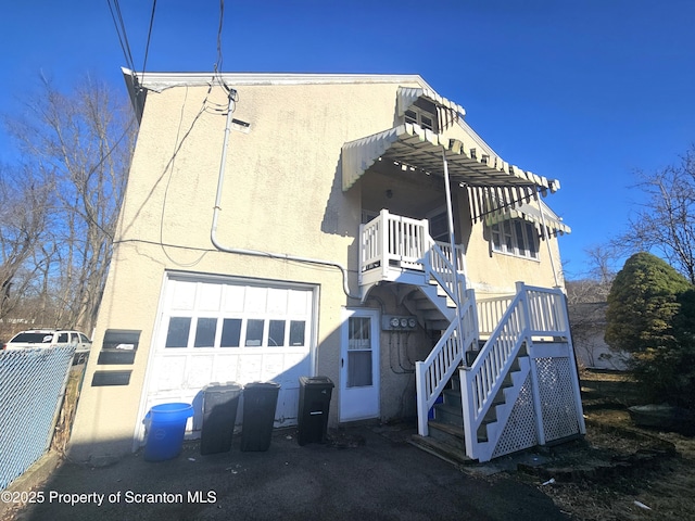 exterior space with stucco siding, an attached garage, stairs, and fence