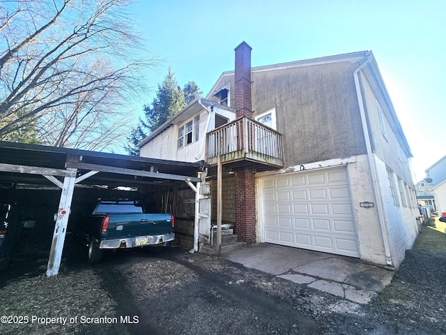 view of home's exterior featuring stucco siding, a balcony, an attached garage, a carport, and a chimney