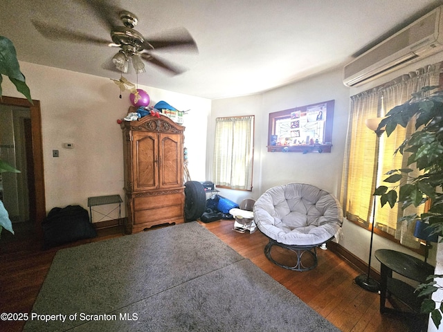 living area featuring a ceiling fan, an AC wall unit, wood finished floors, and baseboards