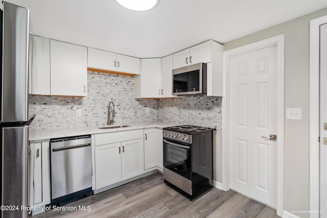 kitchen with white cabinetry, sink, stainless steel appliances, tasteful backsplash, and light wood-type flooring