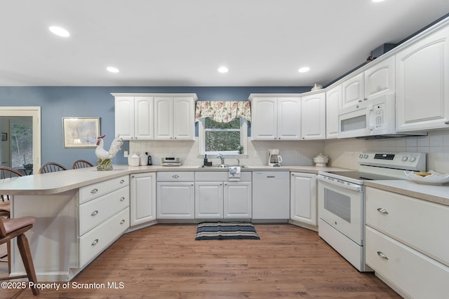 kitchen featuring a sink, a peninsula, white appliances, and tasteful backsplash
