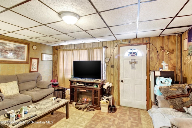 living area featuring a paneled ceiling and wood walls