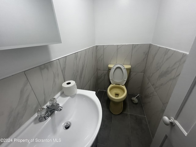 bathroom with toilet, tile walls, and sink