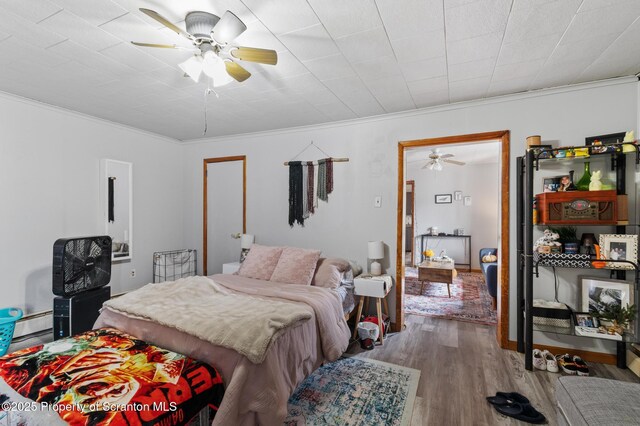 bedroom featuring a baseboard heating unit, wood finished floors, ceiling fan, and ornamental molding