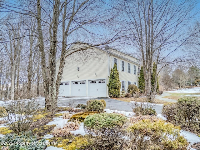 view of snowy exterior featuring driveway and an attached garage