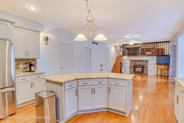 kitchen featuring a center island, a fireplace, light wood finished floors, visible vents, and freestanding refrigerator