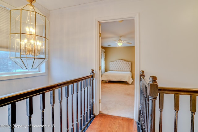 hallway featuring ornamental molding, light wood-type flooring, a notable chandelier, and an upstairs landing