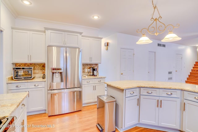 kitchen with stainless steel refrigerator with ice dispenser, hanging light fixtures, light wood-style flooring, backsplash, and light stone countertops